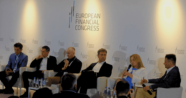 Panel składający się z sześciu osób, pięciu mężczyzn i jednej kobiety, siedzi i prowadzi dyskusję na scenie Europejskiego Kongresu Finansowego. Znajdują się na tle logo i tytułu wydarzenia. Na stole przed nimi stoi woda butelkowana, a widzowie są widoczni.