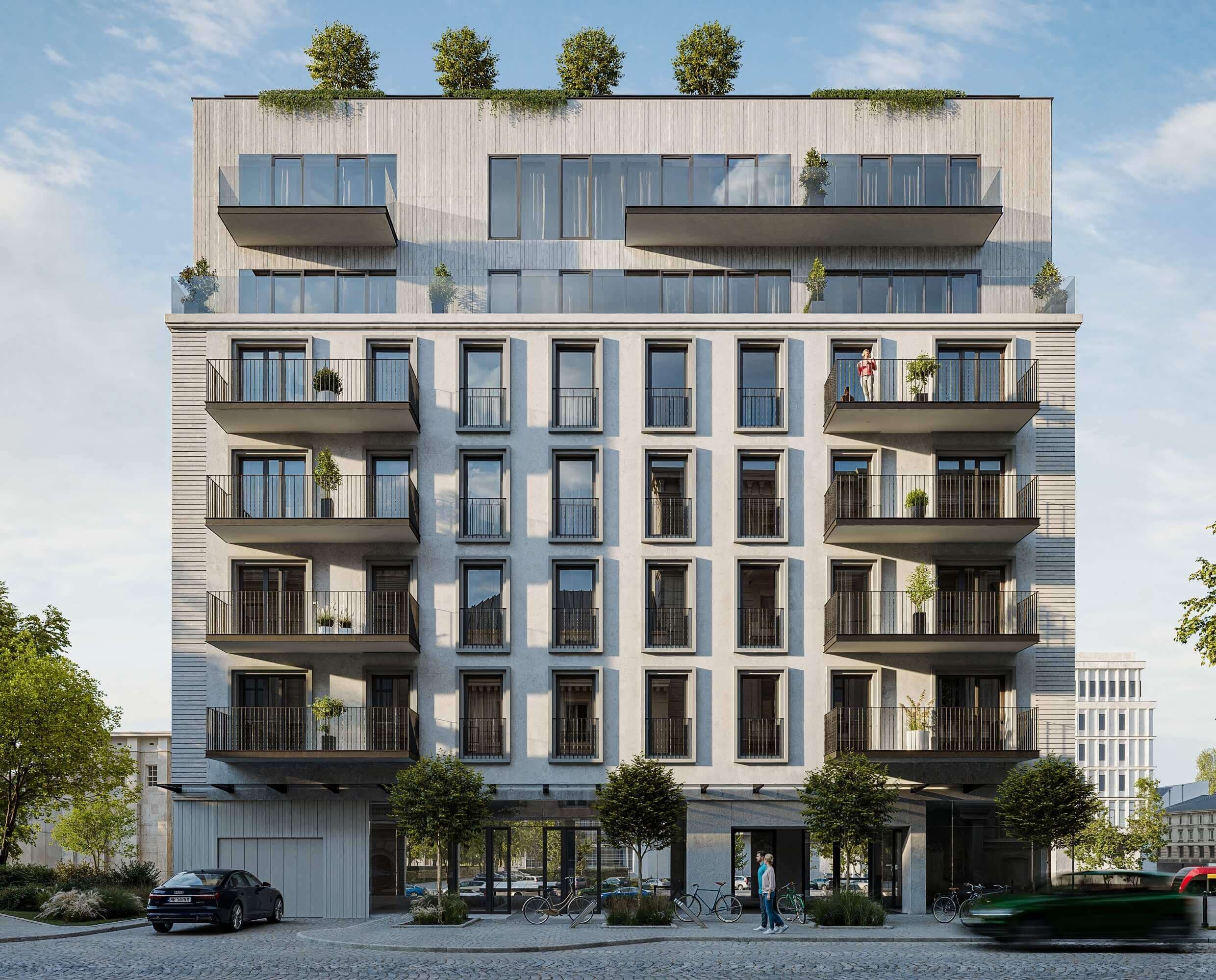 Nowoczesny budynek apartamentowy z sześcioma piętrami, z dużymi oknami i balkonami. Dach jest zielony, a drzewa rosną wzdłuż ulicy przed nim. Na balkonie i na parterze widać ludzi, a na ulicy przejeżdża samochód.